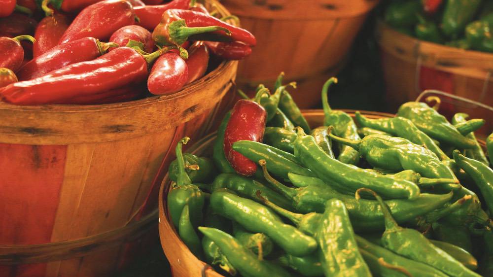 Bushel baskets overflowing with red and green chile peppers at a farm stand